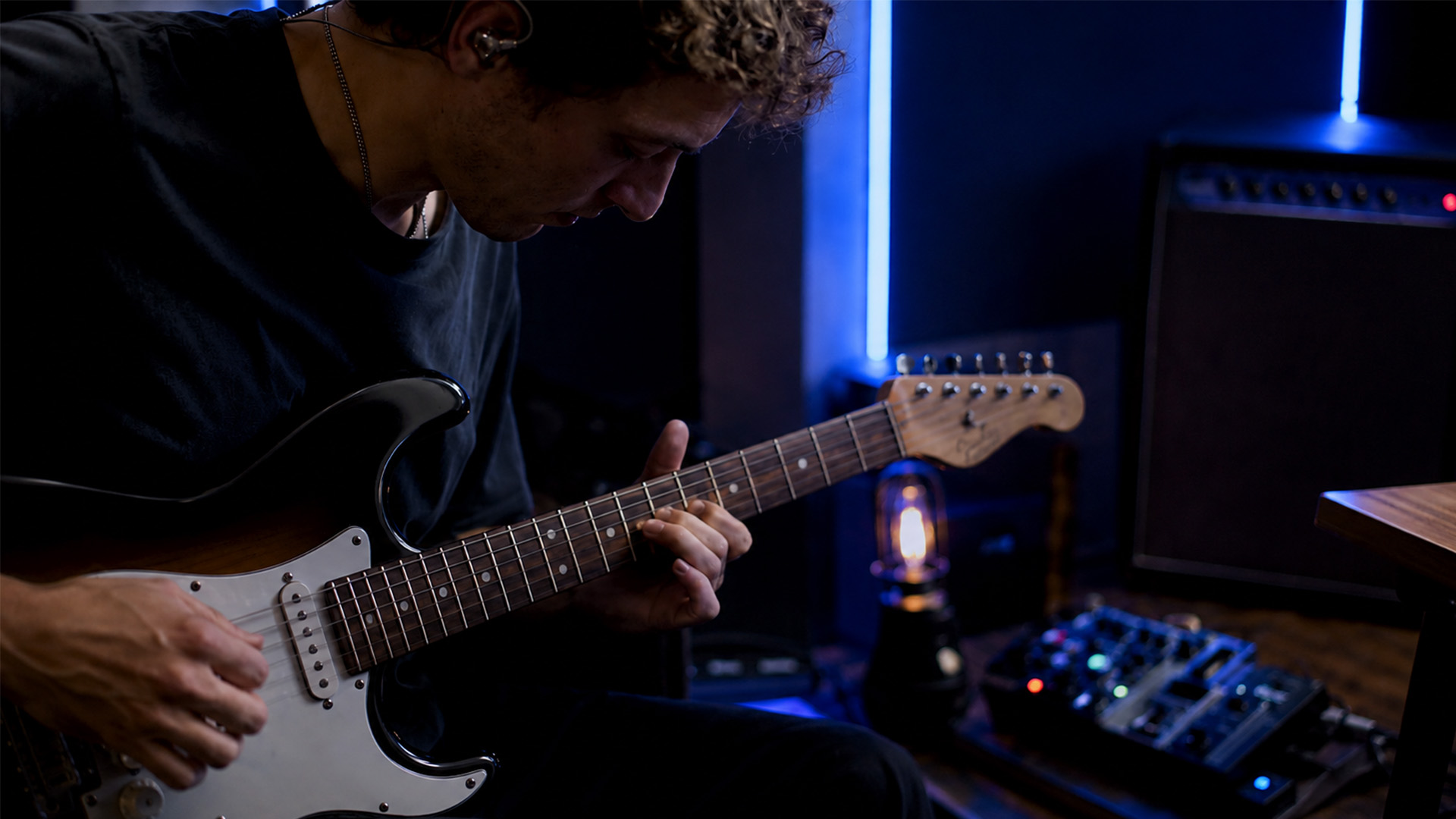 A musician playing a guitar using in-ear monitors